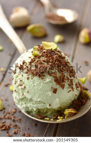 Scoop of homemade pistachio ice cream with chopped pistachios and chocolate on old wooden background