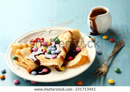 Homemade crepes with multicolored dragee. and chocolate sauce on blue wooden background