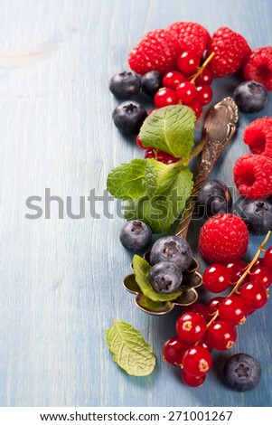 Berries on Blue Wooden Background. Summer or Spring Organic Berry over Wood. Raspberries, Blueberry, Red Currant, Vintage Spoon and Mint. Agriculture, Gardening, Harvest Concept. Copy space.