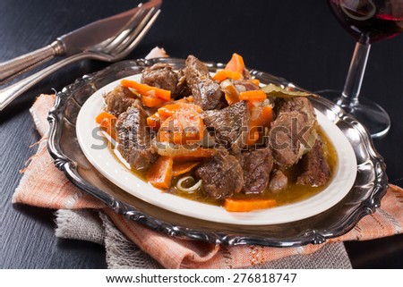 Plate of beef stew with a green salad on dark background. Very Shallow depth of field.