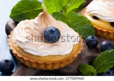 Handmade little tarts, cakes, tartlets with lime curd, meringue en berries on old rusti? board on blue wooden background. Selective focus.