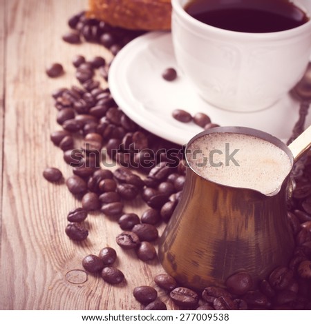 Old coffee pot, cup of coffee and coffee beans on wooden rustic background. Selective focus. Square photo. Retro style toned.