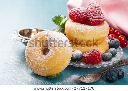 Morning breakfast with mini donuts and berries on plate under powdered sugar on blue wooden background.  Tasty donuts closeup. Doughnut. Selective focus.
