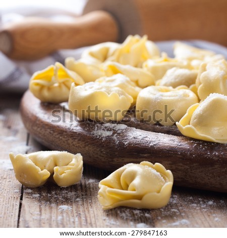 Homemade raw Italian tortellini on wooden vintage cutting board with a rolling pin. Selective focus.