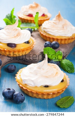 Handmade little tarts, cakes, tartlets with lime curd, meringue en berries on old rustik board on blue wooden background. Selective focus.