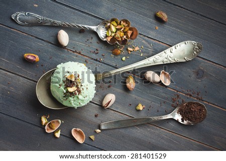 Scoop of homemade pistachio ice cream with chopped pistachios and chocolate on old wooden background. Top view. Retro style toned.