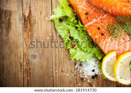 Delicious salmon fillet, rich in omega 3 oil, aromatic spices and lemon on fresh lettuce leaves on rustic wooden background. Healthy food, diet and cooking concept. With copy space. Top view.
