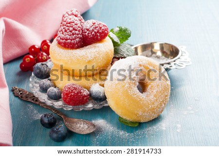 Morning breakfast with mini donuts and berries on plate under powdered sugar on blue wooden background.  Tasty donuts closeup. Doughnut.