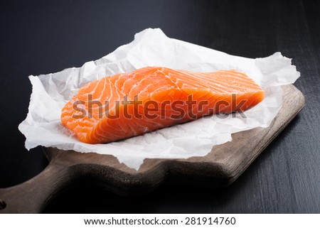 Delicious salmon fillet, rich in omega 3 oil on vintage cutting board on black wooden background. Healthy food, diet and cooking concept.