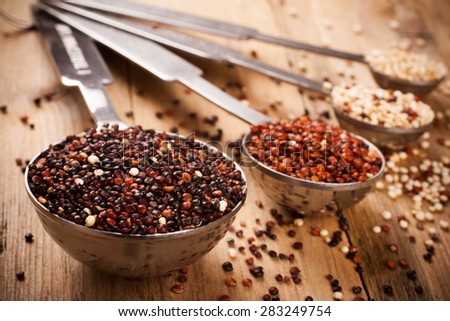 White, red, black and mixed raw quinoa, South American grain, in metal measuring spoons on old wooden background. Healthy food concept. Selective focus.  Retro style toned.
