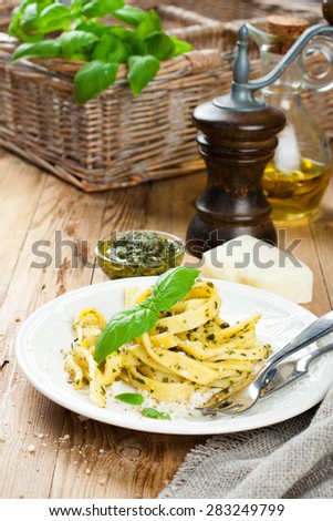 Cooked homemade tagliatelle pasta with green pesto sauce, grated pecorino cheese and basil on white plate on old wooden background.