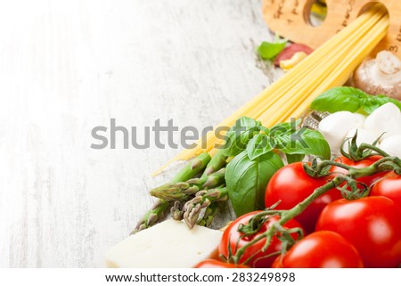 Italian food background, with tomatoes, basil, spaghetti, mushrooms, mozzarella balls, olive oil, spaghetti meter on vintage white wooden table. Copy space. Healthy food concept,