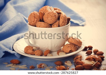 Italian almond cookie amaretti in white coffee cup with almonds on white table with blue napkin, selective focus. retro style toned.