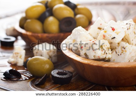 Cubed feta cheese with olives in olive wood bowl and green and black olives on rustic wooden background.  Selective focus.