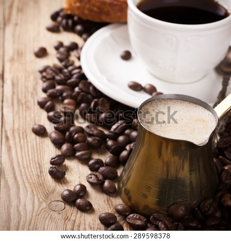 Old coffee pot, cup of coffee and coffee beans on wooden rustic background. Selective focus. Square photo