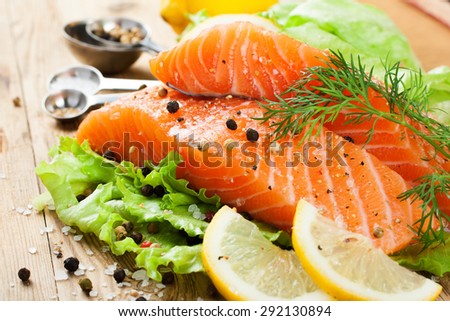 Delicious salmon fillet, rich in omega 3 oil, aromatic spices and lemon on fresh lettuce leaves on rustic wooden background. Healthy food, diet and cooking concept.