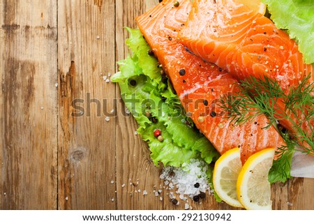 Delicious salmon fillet, rich in omega 3 oil, aromatic spices and lemon on fresh lettuce leaves on rustic wooden background. Healthy food concept. With copy space.  Top view.
