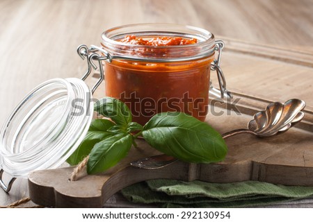 Glass jar with homemade classic spicy tomato pasta or pizza sauce with olives and basil. Italian healthy food background.