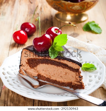 Slice of delicious chocolate mousse cake with cherries and mint on old wooden background. Selective focus.