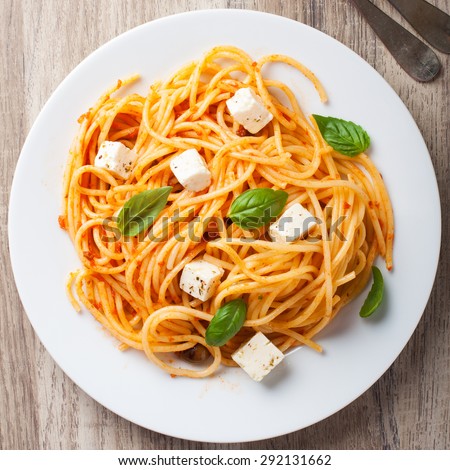 Spaghetti with tomato sauce, feta cheese and basil leaves on white plate on wooden background. Italian healthy food background.