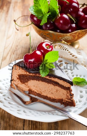 Piece of delicious chocolate mousse cake with cherries and mint on old wooden background. Selective focus.