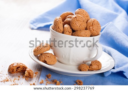 Italian almond cookie amaretti in white coffee cup with almonds on white table with blue napkin, selective focus.