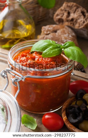 Glass jar with homemade classic spicy tomato pasta or pizza sauce with olives and basil. Italian healthy food background.