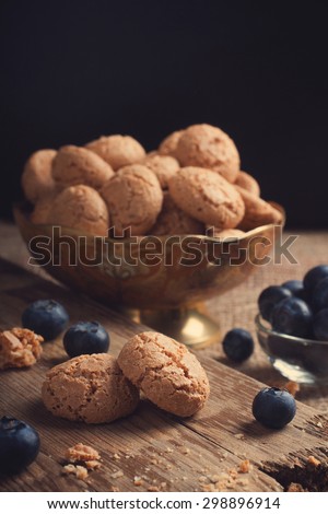 Italian almond cookie amaretti with blueberries on rustic wooden board, selective focus, law key. Toned.