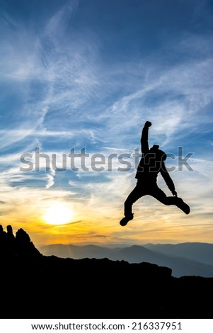 hiker jumps high in the air celebrating success in the sunset