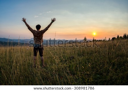 traveller raising his arms in the sunset as a sign of success and freedom