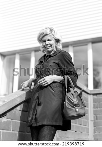 Joyful blonde in a black cloak with a bag down the stairs store. Black and white portrait