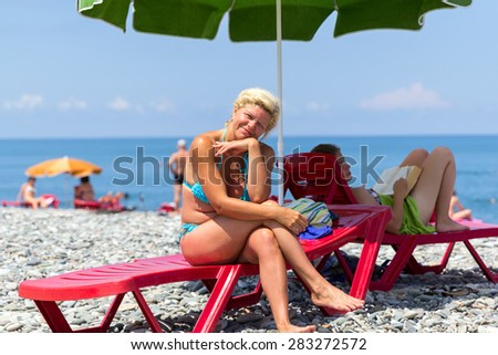 Attractive smiling blonde in blue bikini sitting on deck chair