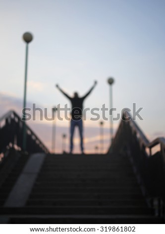Blurred male raising both hands in a victory sign on the top of the stairs