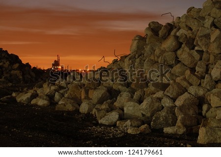 A night view of a pile of demolition debris sits in front of a coal-fired power plant in the background.