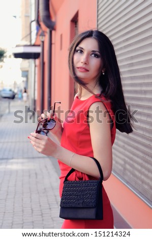 The girl in a red dress and with black glasses in hands turns around on the street
