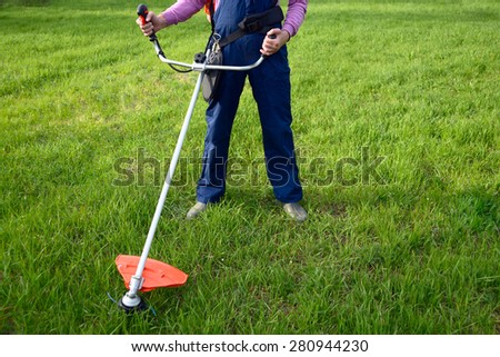 Man wearing ear protectors and glasses mowing grass with petrol weed trimmer