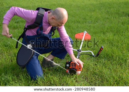 The man starts a weed trimmer on a lawn