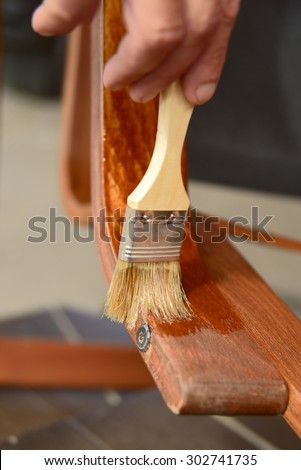 Hand with a brush paints with a varnish a old chair armrest