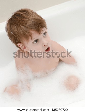 Surprised three years boy in a bathtub with soap foam.