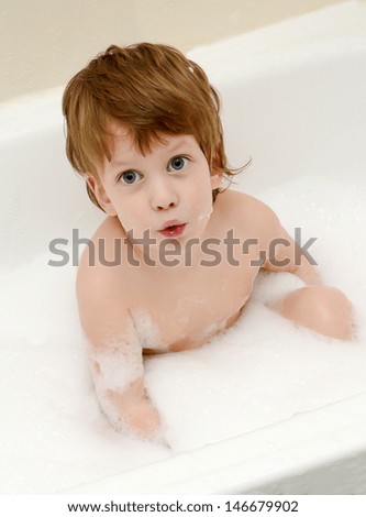 Cute three year old boy taking a bath with foam
