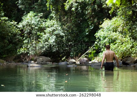 Man trekking through tranquil tropical jungle lagoon in Khao Sok National Park, Thailand
