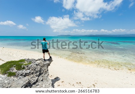 Man standing on rock overlooking impressive tropical beach lagoon paradise in Okinawa, Japan