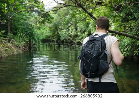 Man trekking through Jungle stream surrounded by dense tropical jungle greenery and vegetation