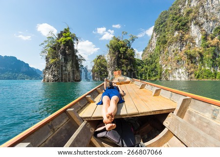 Girl relaxing on boat exploring huge tropical lake with towering limestone cliffs rising from the water in Khao Sok National Park