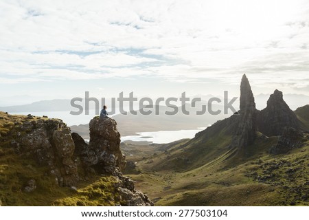 Man sitting on huge rock after challenging climb to mountain summit in the isle of Skye, Scottish highlands, Scotland.