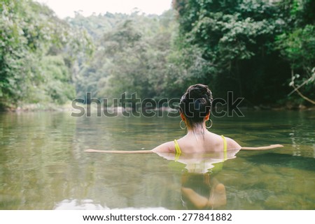 Bikini girl sitting in Jungle lagoon relaxing looking at view of lush Jungle greenery
