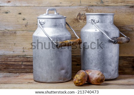 Two potatoes and aluminum old milk cans on a wooden background