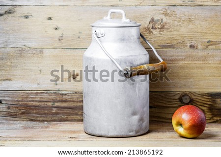 An apple and an aluminum old milk can on a wooden background