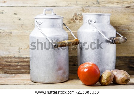 Red tomato, two potatoes and aluminum old milk cans on a wooden background