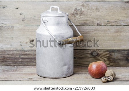 An apple, walnuts and an aluminum old milk can on a wooden background